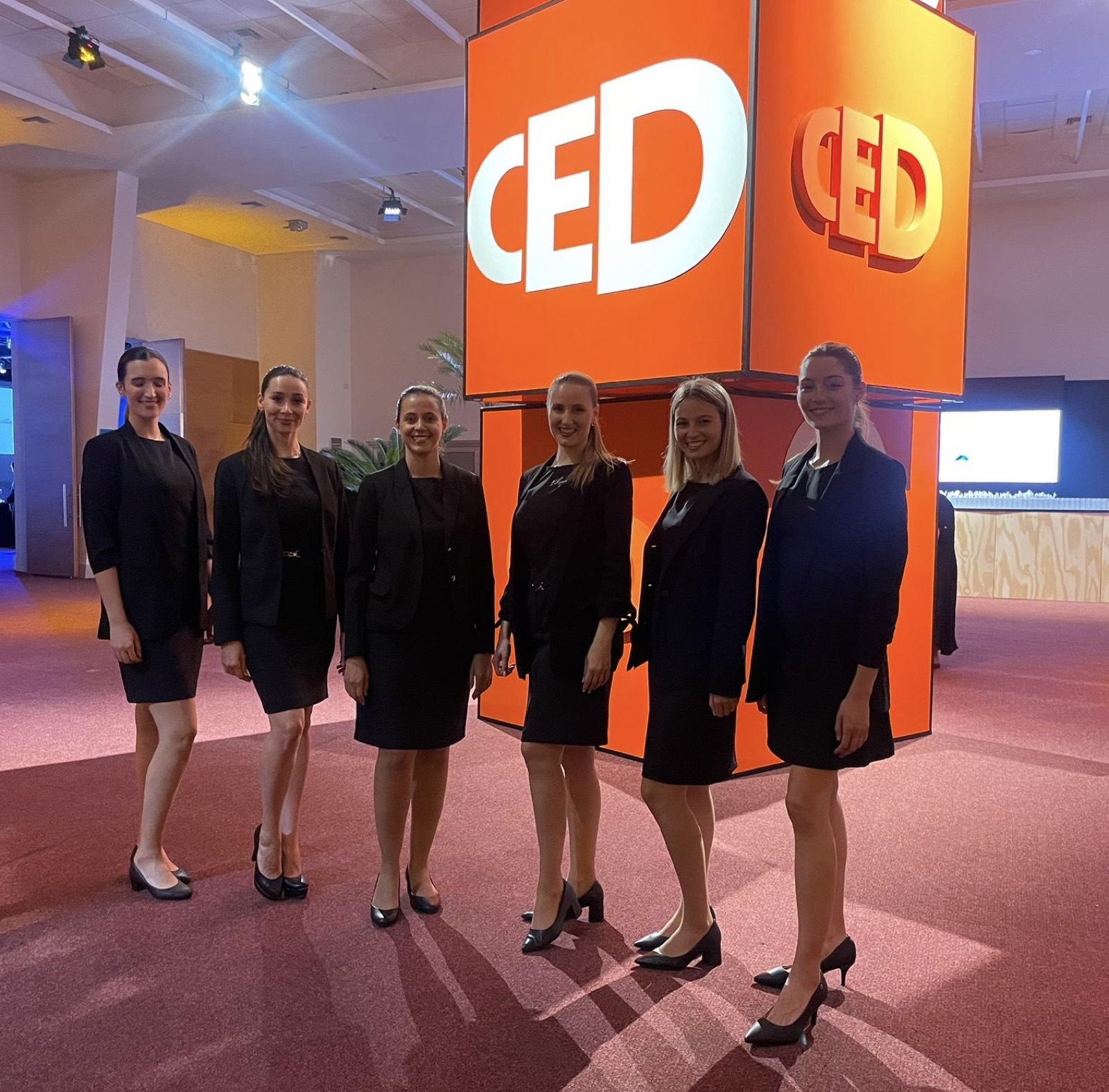 Equipo uniformado de oscuro frente a un fondo naranja en un evento del CED.